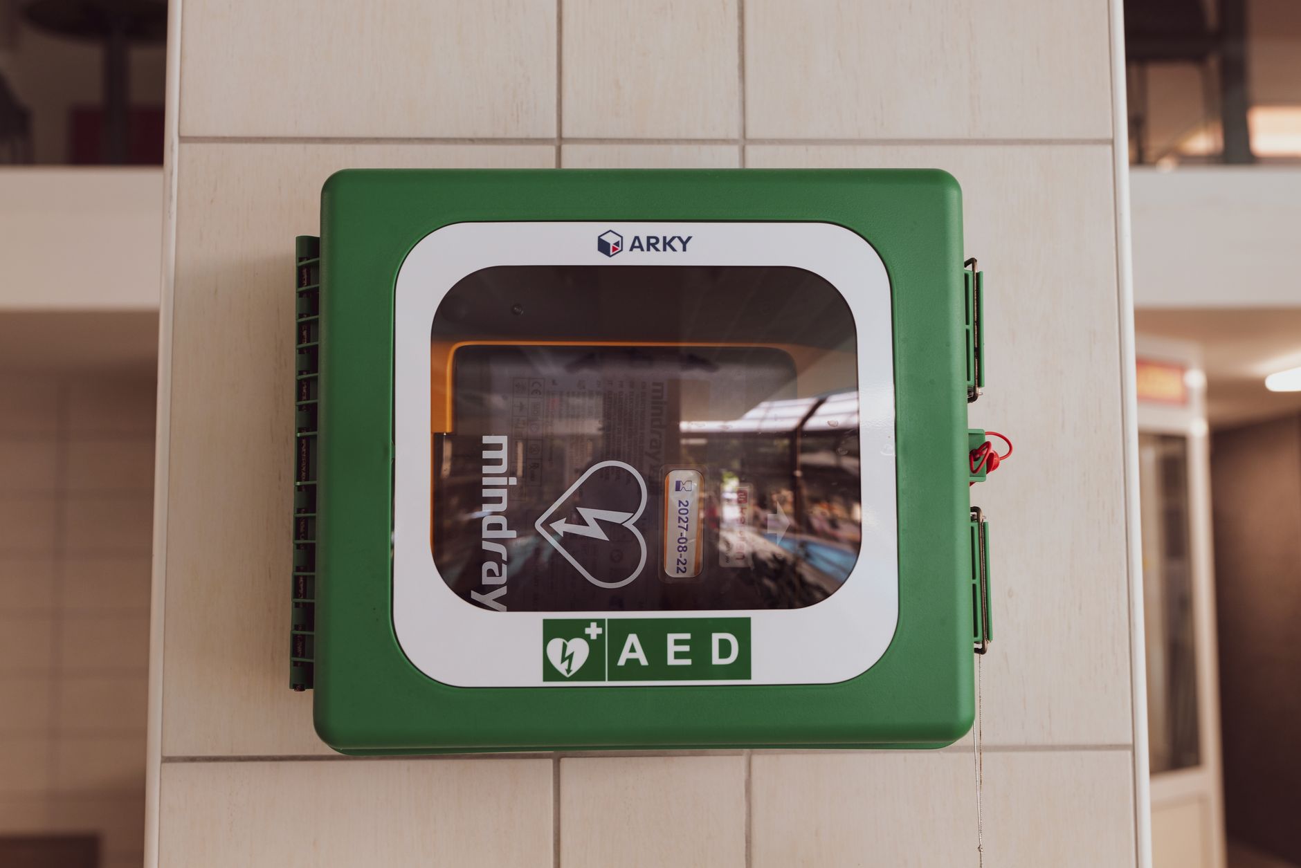 Green defibrillator cabinet on a UK high street wall, illustrating public defibrillator locations UK
